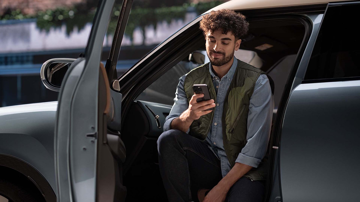 Ein Mann sitzt bei geöffneter Fahrertüre in einem MINI mit einem Smartphone in der Hand